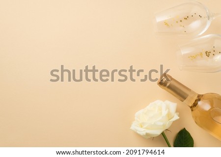Top view photo of white rose two wineglasses with golden sequins and bottle of white wine on isolated beige background with copyspace