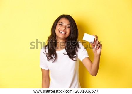 Image of lovely african-american woman smiling happy, showing credit card, standing over yellow background
