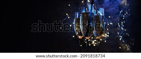 Celebrate with sparkling champagne. Blue illuminated champagne glasses with fairy lights against horizontal black background for new year and party.