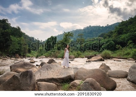 Beautiful asian woman in white dress standing on stone of natural rapids in the valley Royalty-Free Stock Photo #2091830920