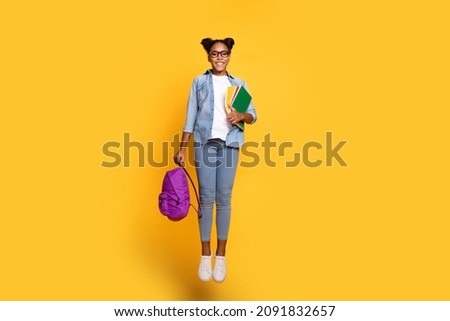 Full size photo of young african lady active hold book bag college jump up isolated over yellow color background