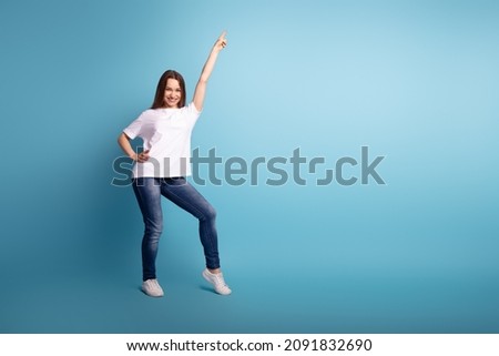 Full size photo of young attarctive girl good mood indciate finger empty space ads isolated over blue color background