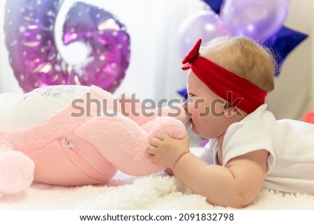 A newborn girl in a red skirt and a red bow on her head is lying on the bed next to a plush toy rabbit. Baloons, Infante, baby, birthday, innocence. toddler, Mother's Day, March 8th. Parents, family