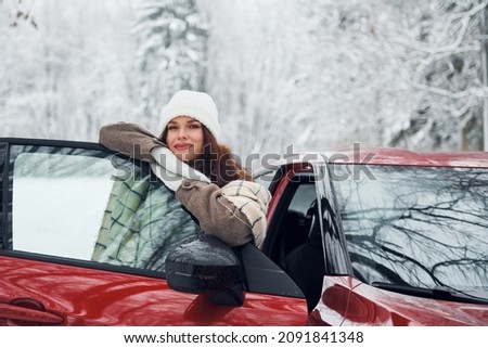Walking out off car. Beautiful young woman is outdoors near her red automobile at winter time.