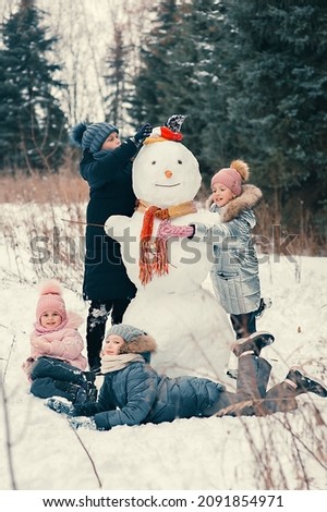 Girls playing with a snowman in the winter snowy forest