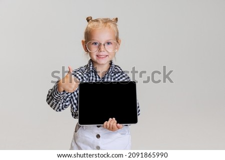 Online education. Cute little girl with tablet isolated over gray background. Boss kid. Model wearing checkered shirt and glasses. Concept of childhood, education, motherhood. Copy space for ad