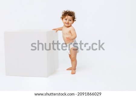 Portrait of little cute toddler boy, baby in diaper cheerfully standing near cube and smiling isolated over white studio background. Concept of childhood, motherhood, life, birth. Copy space for ad Royalty-Free Stock Photo #2091866029