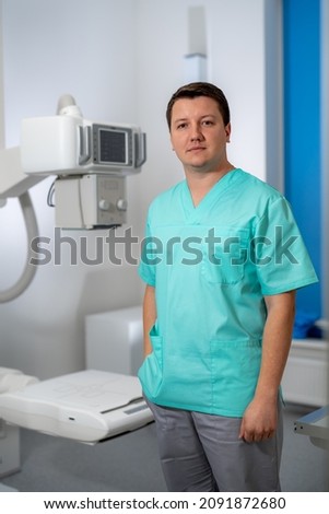 Young serious competent male doctor looking at the camera at doctor's office. Computer tomography background. Stock photo