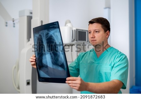 Young serious competent male doctor looking at X-ray at doctor's office. Computer tomography background. Stock photo