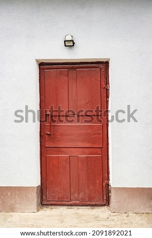 A brown old door and a white wall hangs a lamp on it in the bright time of the day. Depressive picture