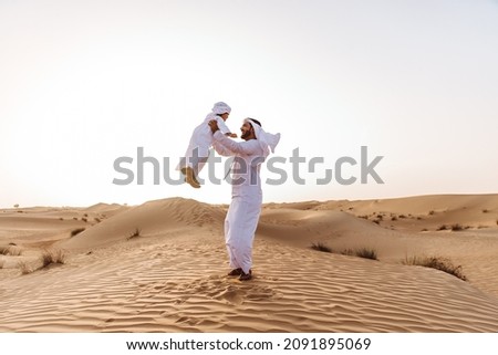 Father and son spending time in the desert on a safari day. Arabian family from the emirates wearing the traditional white dress. Concept about lifestyle and middle eastern cultures Royalty-Free Stock Photo #2091895069