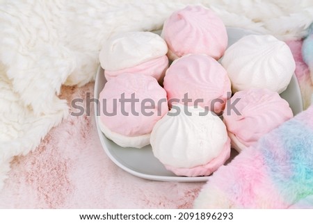 Russian dessert zefir or zephyr on white plate, colorful and white fur scarves on pink background. Marshmallow closeup picture.