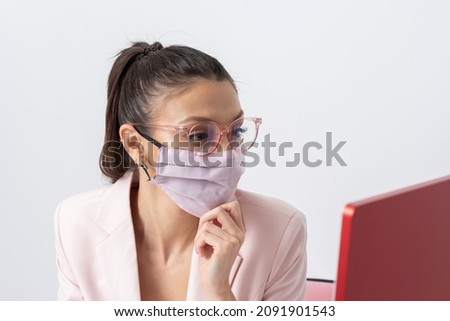 Salisbury, Wiltshire, UK. 2021. Attractive woman wearing pink facemask and using a computer and keyboard.