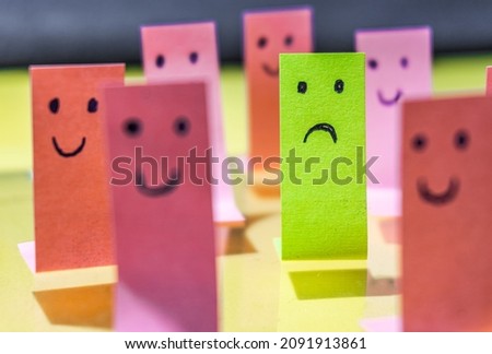 Smiley faces painted on pink stickers, highlighting a sad face on a green sticker. Concept of feeling different, not fitting into society. Royalty-Free Stock Photo #2091913861