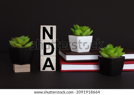NDA. text on wooden cubes. On a black background. red notepad. plant in the pot