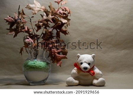 a toy polar bear sits under dry maple leaves. space for printing. background picture.