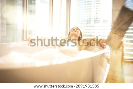 Beautiful woman taking hot bath in a luxury bathroom. Young lady taking care of her body and skin in a rooftop apartment.