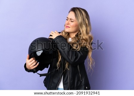 Young Brazilian woman holding a motorcycle helmet isolated on purple background suffering from pain in shoulder for having made an effort