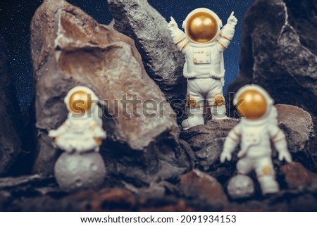 Astronaut with gold visor and White Spacesuit on rock surface with space background. One astronaut on the moon sitting and meditating while another astronauts celebrating success.