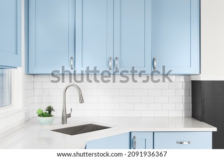 Detail of a kitchen with light blue cabinets, white granite countertop, subway tile backsplash, and a light hanging above a window. Royalty-Free Stock Photo #2091936367