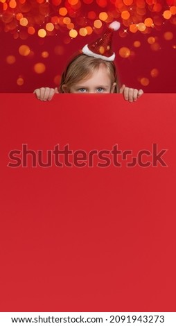 vertical red new year billboard with bokeh and christmas lights, with space for large copies. A little girl looks out from behind a red background and looks with cheerful eyes, her face is not visible