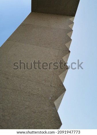 Carved stone wall isolated on blue sky background. Hewn granite or marble structure with zigzag profile. Abstract architecture. Modern architectural detail. Geometric structure with polygonal pattern.