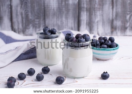 A healthy breakfast of Greek yogurt in glass jars and fresh blueberries at a rustic white table. Selective focus on glass jar