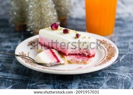 Sweet mousse cake on vintage plate in cut and decorative christmas tree and glass of juice on gray background.