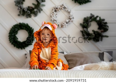 A cute boy in tiger cubs costumes play on the bed.Blond boy in pajama playing in bed.The symbol of the new year is a tiger.A child in kigurumi pajamas in a New Year theme 