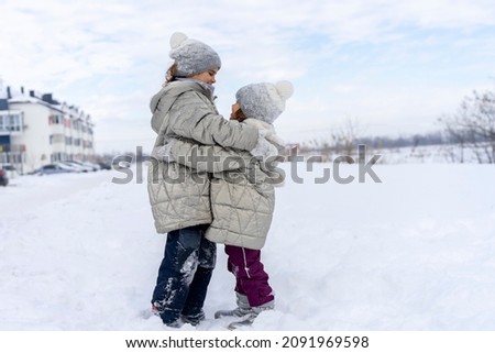 Funny girls hugging in the winter in the snow. Happy sisters play snow games. Children Friends are happy to be together on a cold winter day