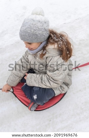 Happy children ride sled riding together behind a car. Funny sisters play snow games in ride attraction. Cheerful kids on a snowy slide. Cute child having fun at winter holidays