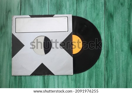 Aged black paper cover and vinyl LP record isolated on green background