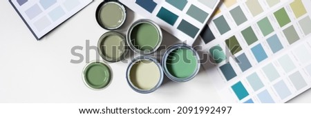 Tiny sample paint cans during house renovation, process of choosing paint for the walls, different green colors, color charts on background, banner size Royalty-Free Stock Photo #2091992497