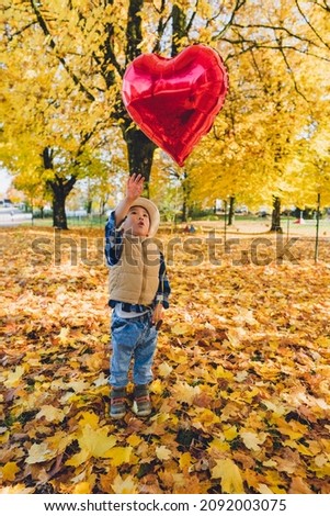 A boy reaching a heart shape balloon in autumn