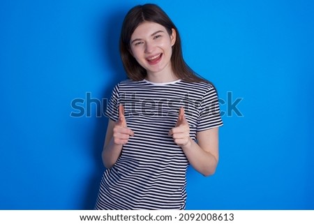 Caucasian woman wearing striped T-shirt isolated over blue background directs fingers at camera selects someone. I recommend you. Best choice