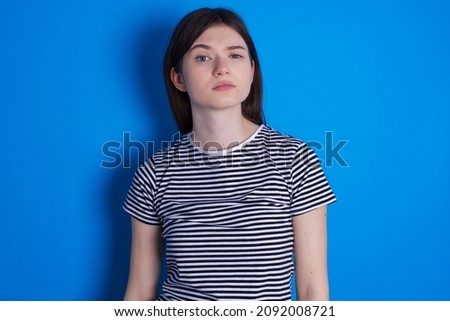 Displeased Caucasian woman wearing striped T-shirt isolated over blue background frowns face feels unhappy has some problems. Negative emotions and feelings concept
