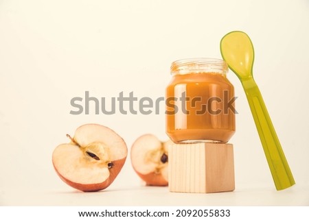 baby puree in a transparent glass jar on a white background. fruit baby puree with spoon. jar of baby puree with fruit