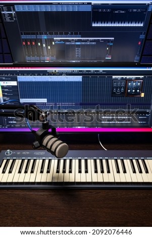 Professional studio condenser microphone in modern music recording studio with computer screen showing user interface of digital audio workstation software with track song