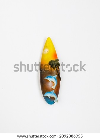 Magnetic Souvenir from Egypt, Thailand, Sri Lanka or Bali. Surfboard with sea, dolphins and palms on white fridge background. Tropical, surfing travel concept. Top view, flat lay, vertical, close up