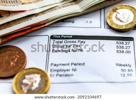 A payslip showing pay as you earn tax deductions, national insurance and pension contributions with some bank notes and coins. Royalty-Free Stock Photo #2092104697