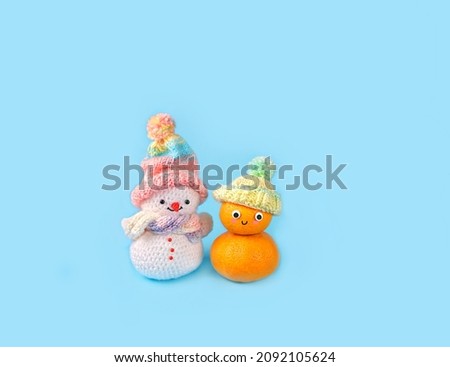 knitted snowman and snowman made of orange tangerines on blue background. Friendly Face funny character. kawaii style. Christmas, New Year holidays, festive winter season.