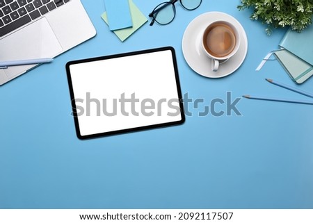 Top view digital tablet, coffee cup, sticky notes and laptop on blue background.