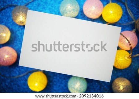 Empty paper card mockup and LED cotton balls decoration on blue bokeh background