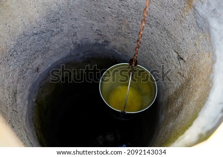Metal bucket in draw-well in European village. Retro stone water well in rural area Royalty-Free Stock Photo #2092143034