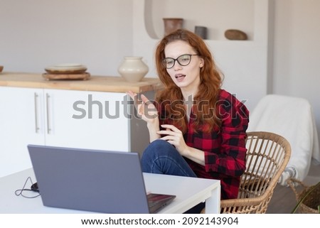 young pretty red-haired girl talking using a computer at home in the kitchen