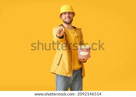 Young man with bucket of popcorn on color background