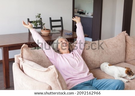 Portrait happy healthy middle aged woman relaxing on comfortable couch at home. Smiling pleasant 50s elderly gray-haired female with dog
