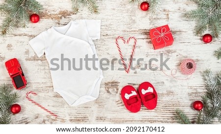 Baby bodysuit kimono mockup on Christmas wooden background with accessories, toys, rattles. Infant clothes mockup with Christmas baubles, candy canes and fir branches.