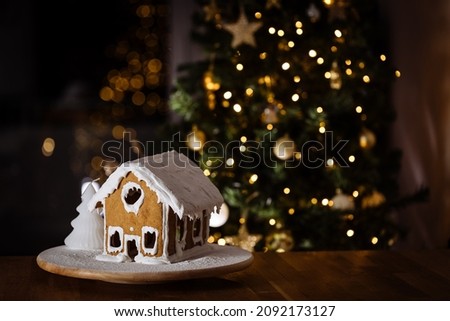 Gingerbread house on a table with Christmas tree in blurry background and reflection. Christmas night. Wonderful holiday mood lights. Decorated in festive atmosphere