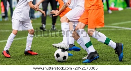 Background image of football game. Legs of soccer players kicking vlack and white soccer ball on artificial grass pitch. Soccer coach on sideline